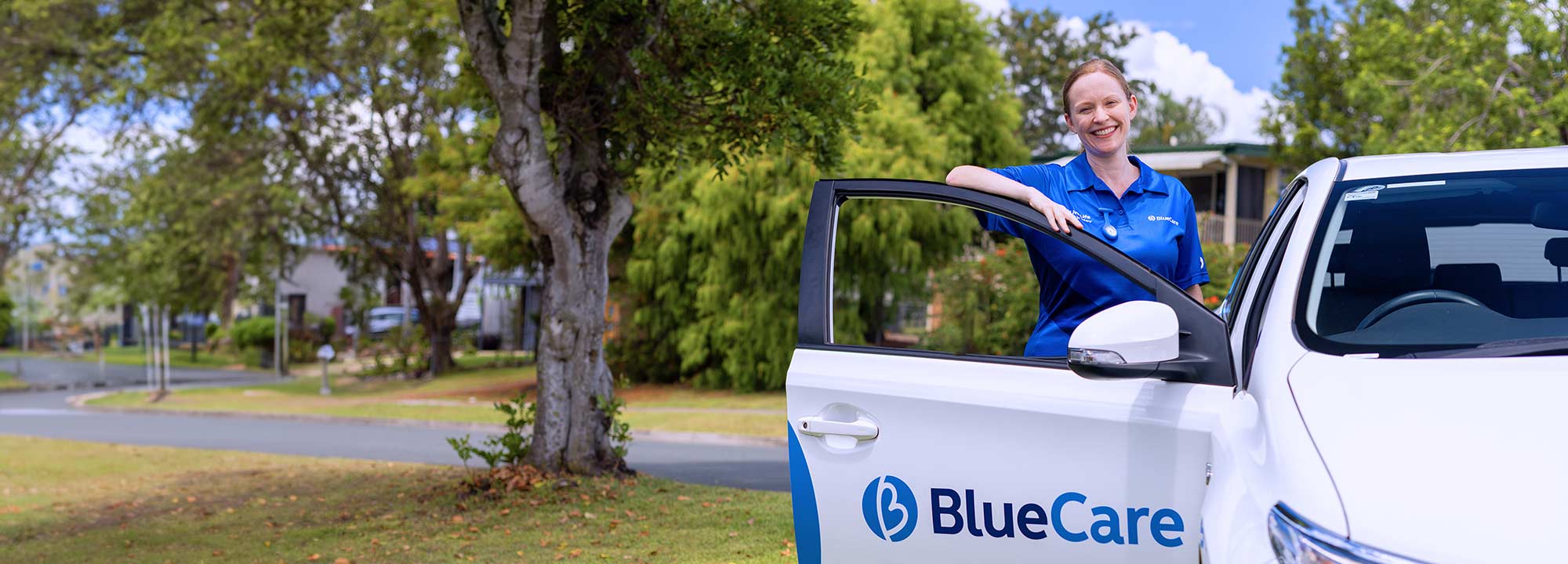 A BlueCare employee standing beside a car with the door open showing the BlueCare logo.